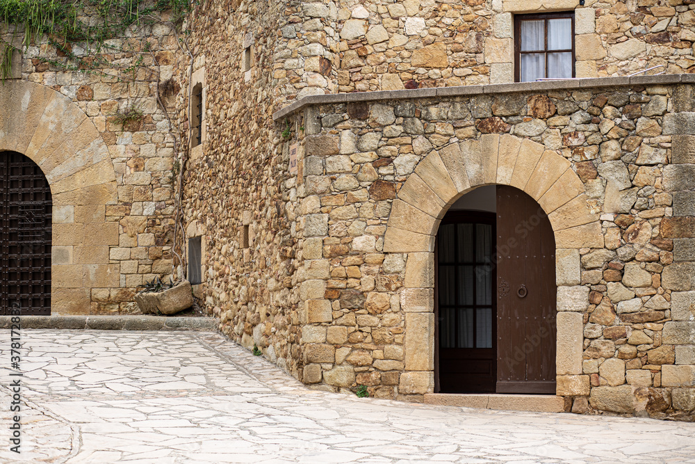 Arc entry facade door on a medieval rock stone building with cobble stones street