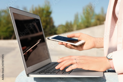 Young woman using phone and laptop outdoors, closeup