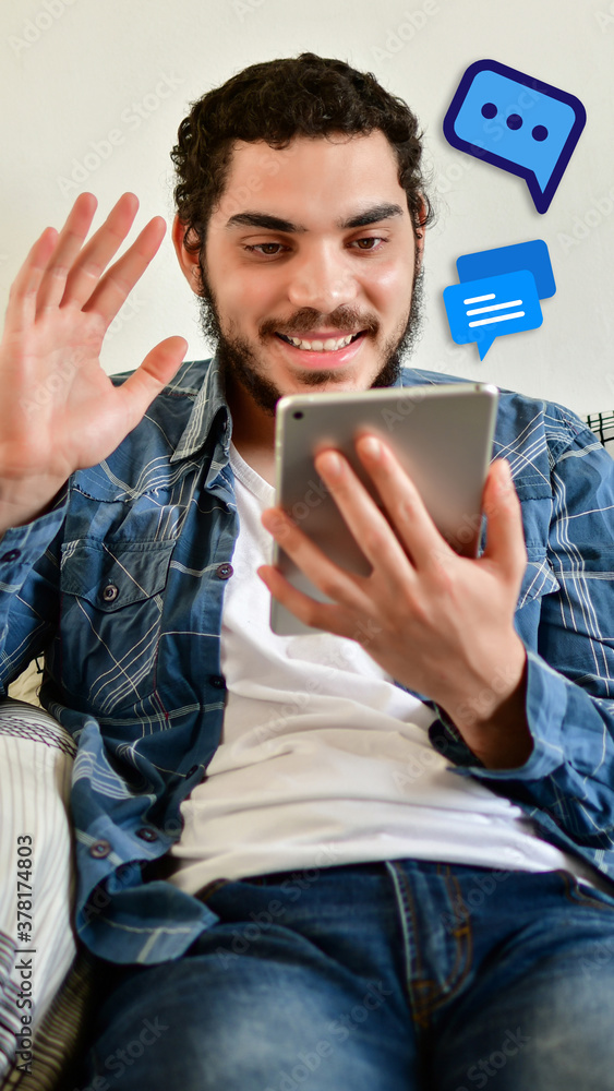 Young man makes video call on his tablet with a friend, lying on Young man makes video call on his tablet with a friend, lying on