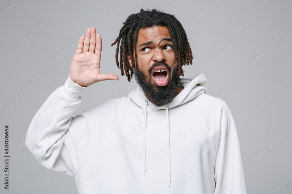 Shocked curious young african american man with dreadlocks 20s in white casual streetwear hoodie posing try to hear you overhear listening intently isolated on grey color background studio portrait. Shocked curious young african american man with dreadlocks 20s in white casual streetwear hoodie posing try to hear you overhear listening intently isolated on grey color background studio portrait.