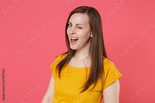 Cheerful beautiful attractive charming blinking young brunette woman 20s wearing yellow casual t-shirt posing standing and looking camera isolated on pink color wall background studio portrait. © ViDi Studio