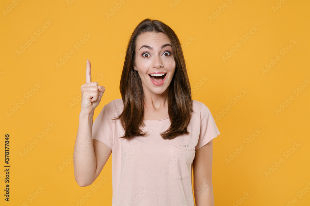 Excited shocked young brunette woman 20s wearing pastel pink casual t-shirt posing holding index finger up with great new idea looking camera isolated on yellow color wall background studio portrait. Excited shocked young brunette woman 20s wearing pastel pink casual t-shirt posing holding index finger up with great new idea looking camera isolated on yellow color wall background studio portrait.