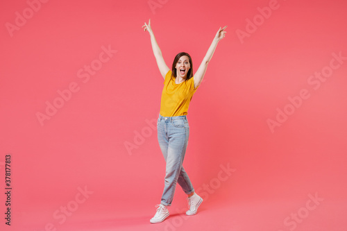 Full length portrait of shocked young brunette woman 20s in yellow casual t-shirt pointing index fingers up on mock up copy space keeping mouth open isolated on pink color wall background studio.