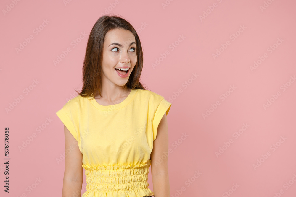 Surprised excited amazed young brunette woman 20s wearing yellow casual t-shirt posing standing keeping mouth open looking aside isolated on pastel pink color wall background studio portrait. Surprised excited amazed young brunette woman 20s wearing yellow casual t-shirt posing standing keeping mouth open looking aside isolated on pastel pink color wall background studio portrait.