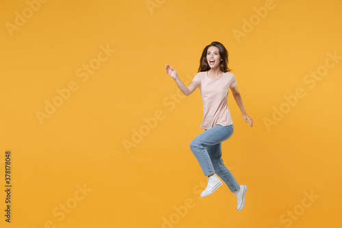 Full length portrait of excited cheerful funny young woman 20s wearing pastel pink casual t-shirt posing jumping like running looking aside isolated on bright yellow color wall background studio.
