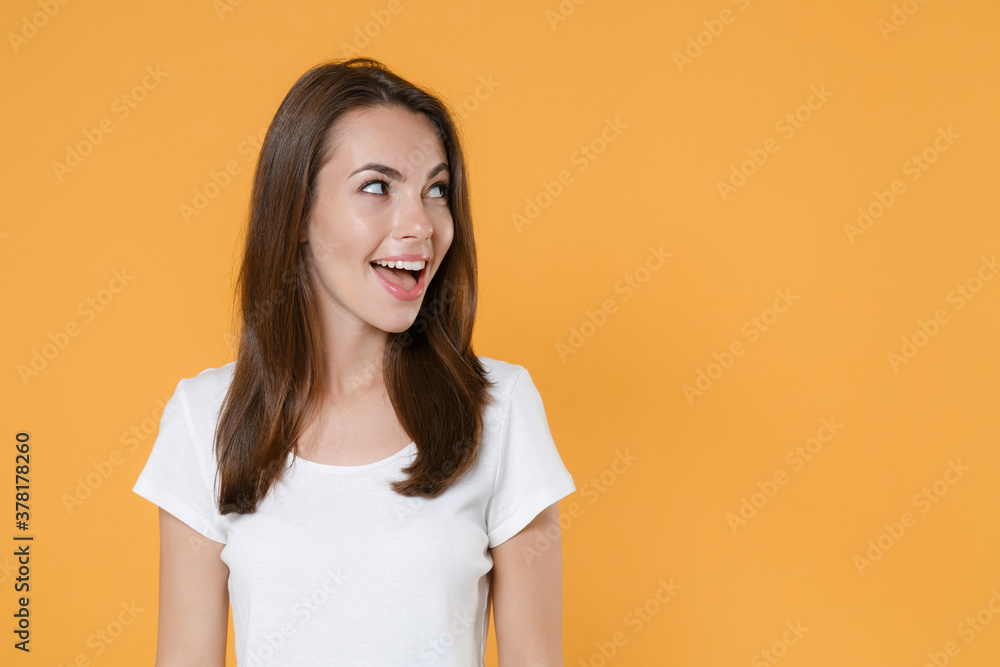 Surprised excited beautiful attractive young woman 20s wearing white blank empty design casual t-shirt posing keeping mouth open looking aside isolated on yellow color wall background studio portrait. Surprised excited beautiful attractive young woman 20s wearing white blank empty design casual t-shirt posing keeping mouth open looking aside isolated on yellow color wall background studio portrait.