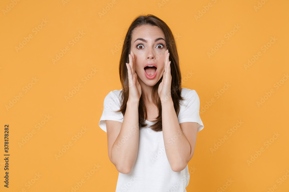Shocked surprised amazed young woman 20s in white blank empty design casual t-shirt posing screaming with hands gesture near mouth looking camera isolated on yellow color background studio portrait. Shocked surprised amazed young woman 20s in white blank empty design casual t-shirt posing screaming with hands gesture near mouth looking camera isolated on yellow color background studio portrait.