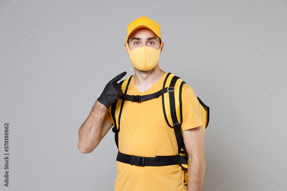Delivery employee man guy in yellow cap t-shirt uniform face mask gloves thermal food bag backpack work courier service during quarantine coronavirus covid-19 virus isolated on gray background studio. Delivery employee man guy in yellow cap t-shirt uniform face mask gloves thermal food bag backpack work courier service during quarantine coronavirus covid-19 virus isolated on gray background studio.