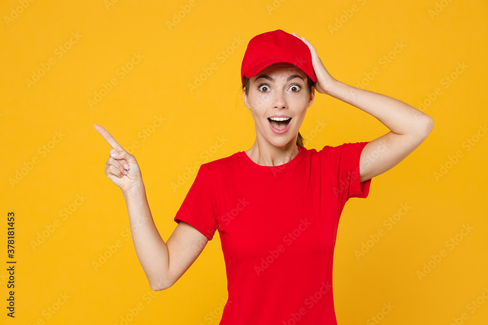 Delivery employee woman in red cap blank t-shirt uniform work courier in service during quarantine coronavirus covid-19 virus, pointing fingers aside on workspace isolated on yellow background studio.