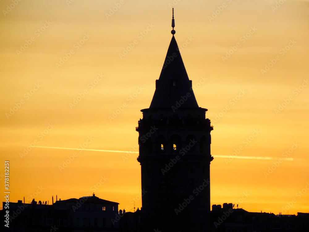 Silueta oscura de Torre Galata en Estambul (Turquia) al atardecer con cielo amarillento que destaca sobre los edificios del centro de la ciudad y parte superior cónica con un mirador y restaurante Silueta oscura de Torre Galata en Estambul (Turquia) al atardecer con cielo amarillento que destaca sobre los edificios del centro de la ciudad y parte superior cónica con un mirador y restaurante