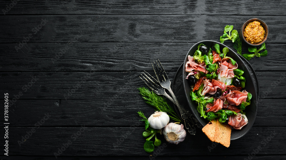 Prosciutto salad with olives in a black bowl. Spanish cuisine. Top view. Free space for your text. Rustic style. Prosciutto salad with olives in a black bowl. Spanish cuisine. Top view. Free space for your text. Rustic style.