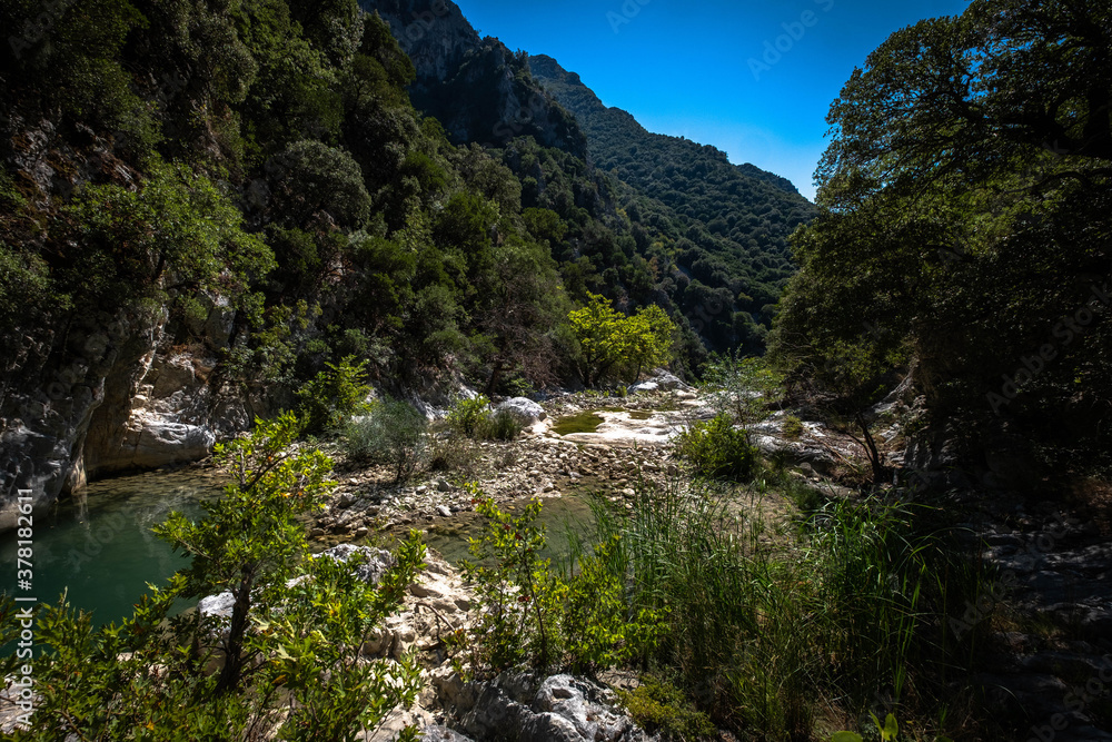 Fototapeta premium Small river enveloped with rocks. Closeup of river scenes in forest in Epirus Greece.