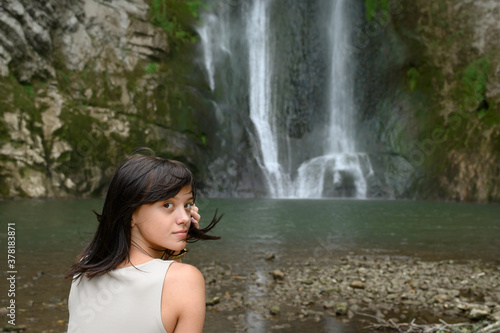 Beautiful young woman sitting in front of waterfall.