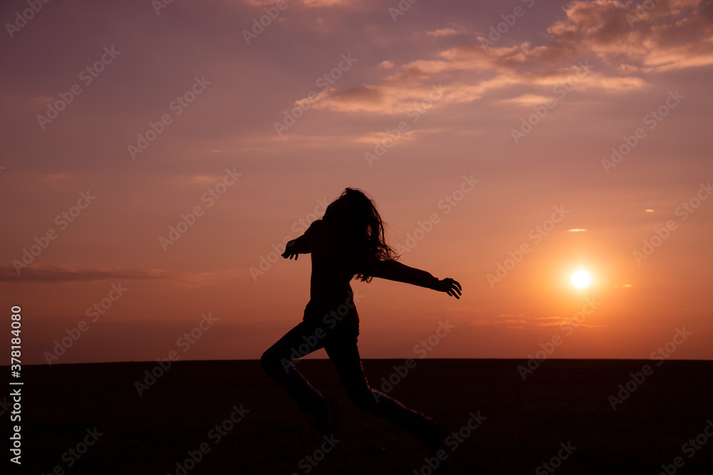 Dark silhouette of a girl with long hair running across a field at sunset
