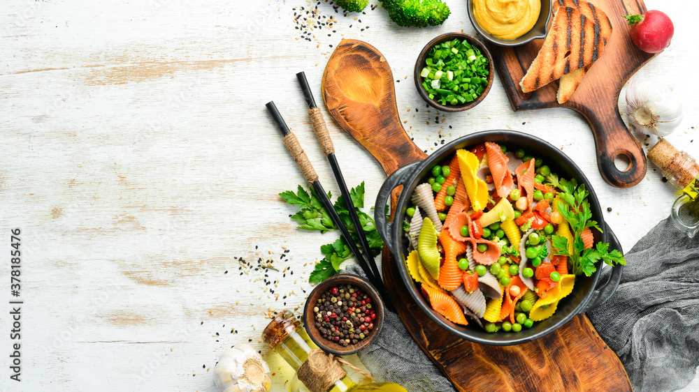 Colored pasta with peas and vegetables in a black bowl. Top view. Free space for text. Colored pasta with peas and vegetables in a black bowl. Top view. Free space for text.