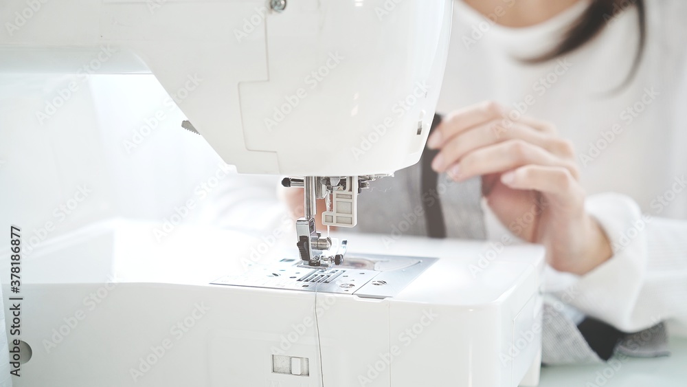 Concept of sewing courses in modern bright studio, sewing in process, blurred background. Female hands sew on a white sewing machine close-up. 