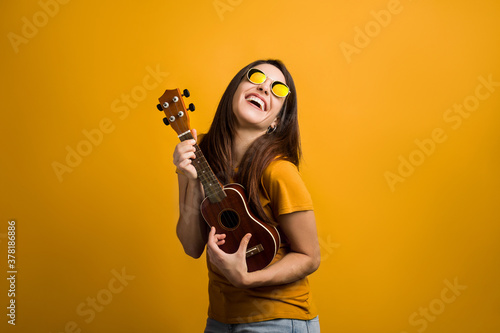 Attractive girl with long hair having fun with ukulele and modern glasses.