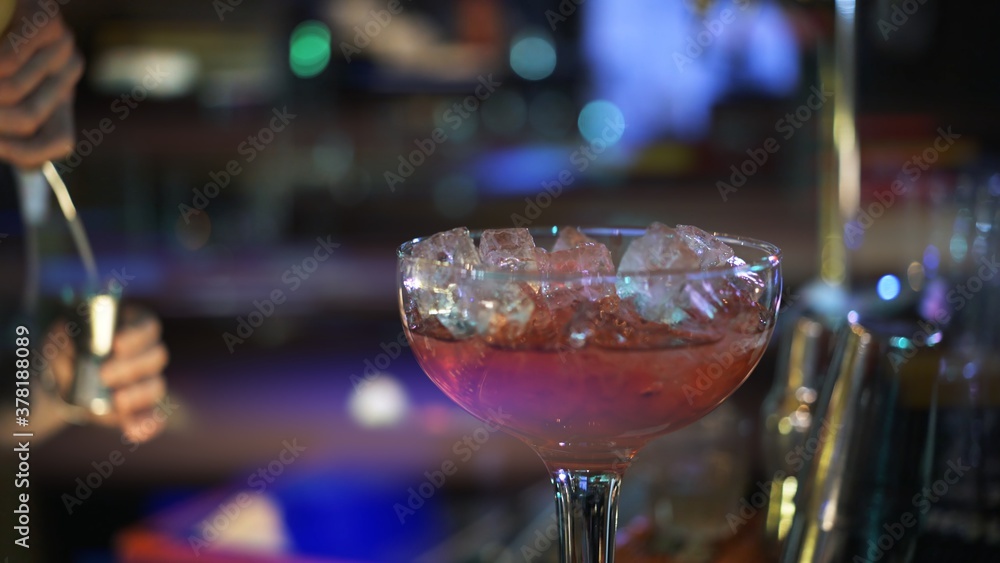 Red cocktail with ice on bar counter, background of night club dark light. Close up of glass with cocktail and ice, concept of cocktail making in night clubs, blurred background