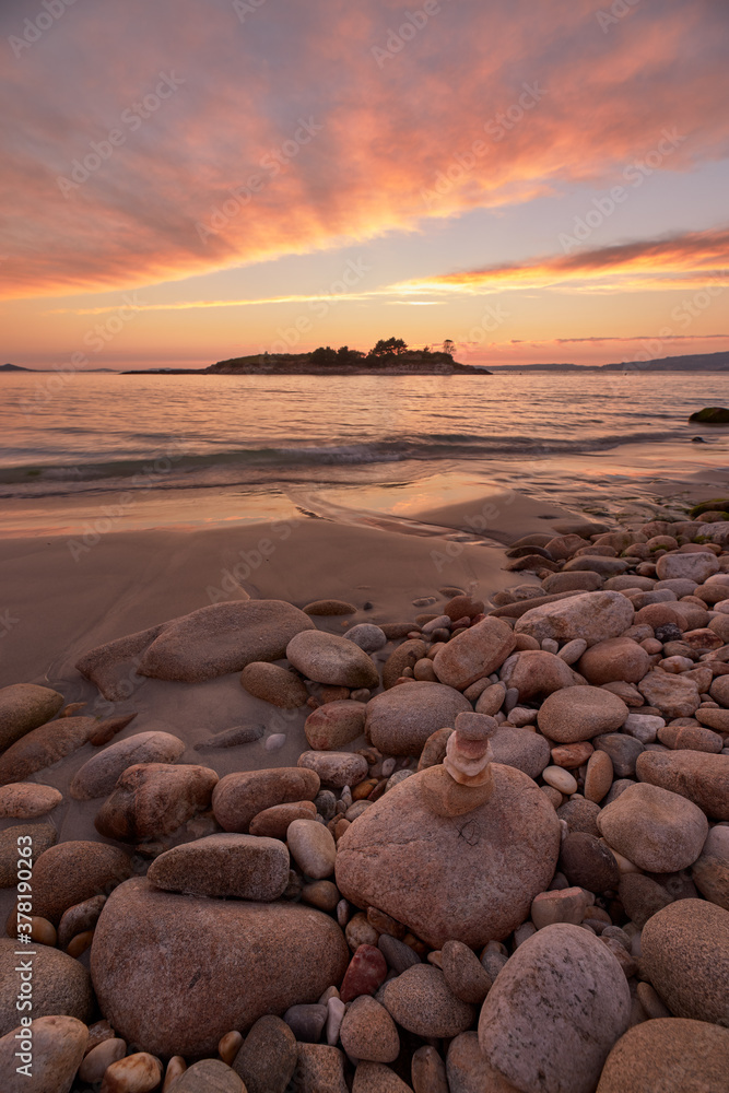 Reddish sunset on round stone beach on the beach called Santo do Mar, in Galicia.