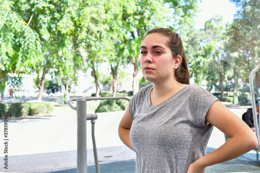 Fototapeta premium Young woman looking into the distance, standing resting in a public park. A sunny day.