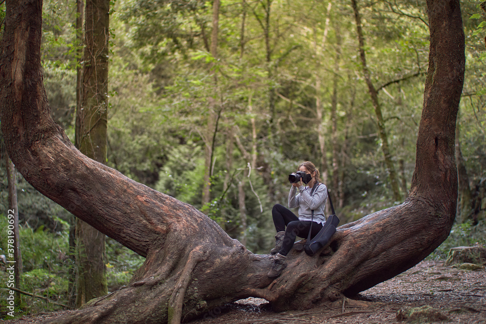 Girl with a mask taking photos sitting on the trunk of a tree. Girl with a mask taking photos sitting on the trunk of a tree.