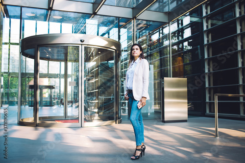 Attractive caucasian woman in trendy formal wear standing near office building looking away, beautiful prosperous female 30s manages dressed in smart casual look posing on urban setting background