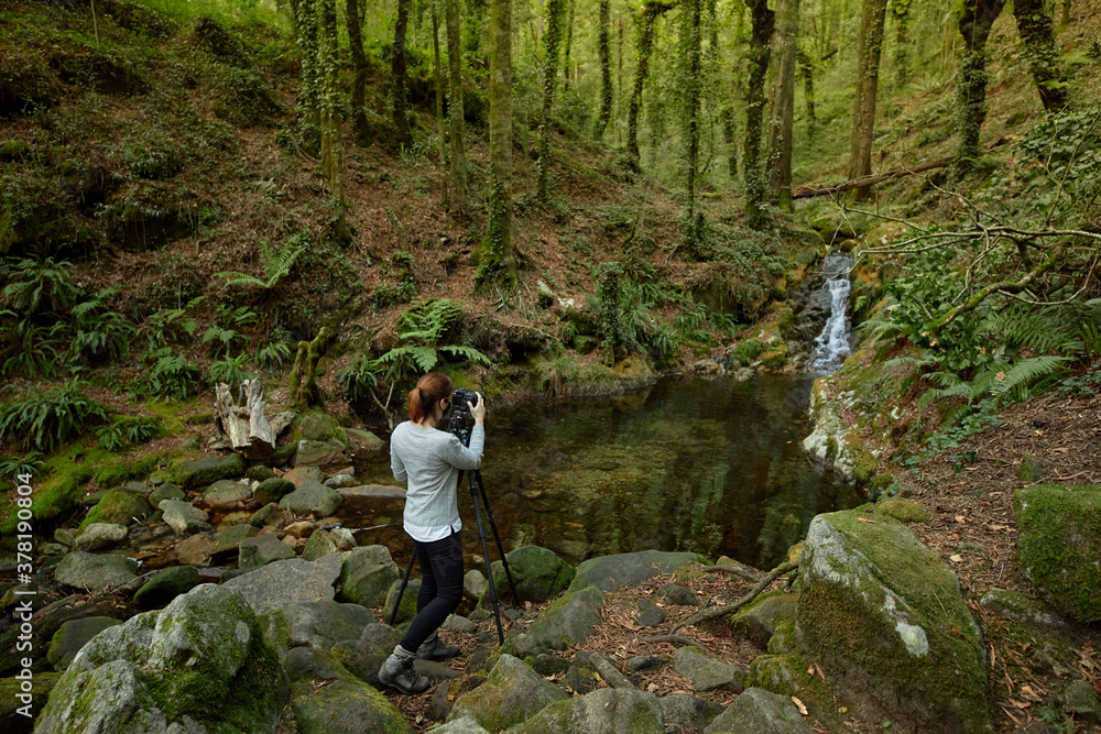 Girl with a mask taking pictures of a river in a forest.