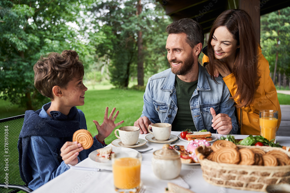Happy parents chatting with son while having breakfast outdoors