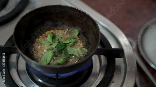 Adding Cardamon And Bay Leaves In A Small Deep Pan Over A High-Flamed Stove. - High Angle Shot photo