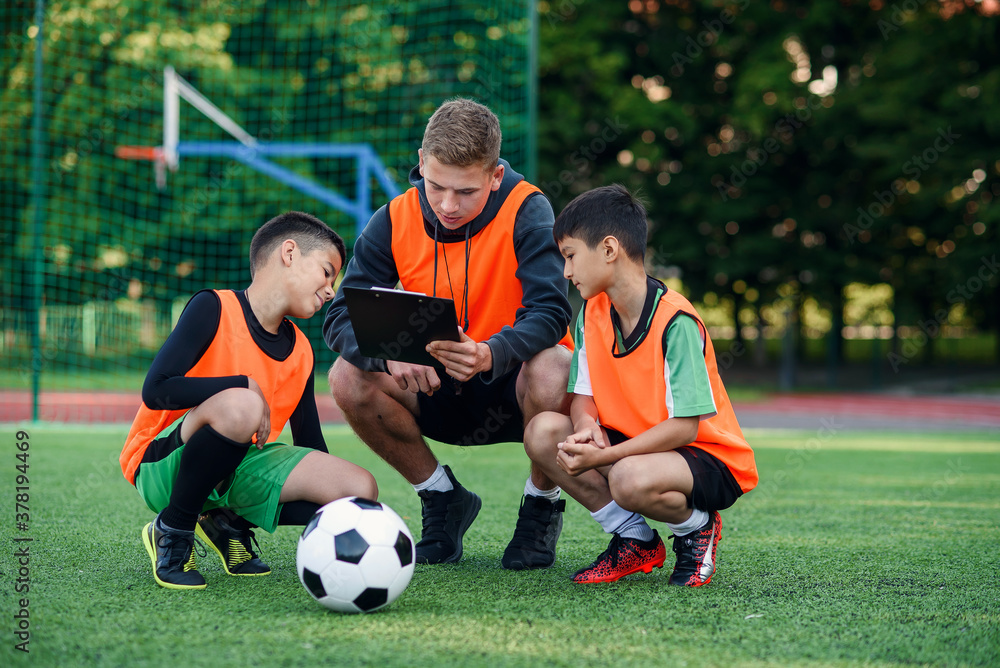 Obraz premium Professional soccer coach tells the strategy of football game to his attentive teen players at stadium during training.