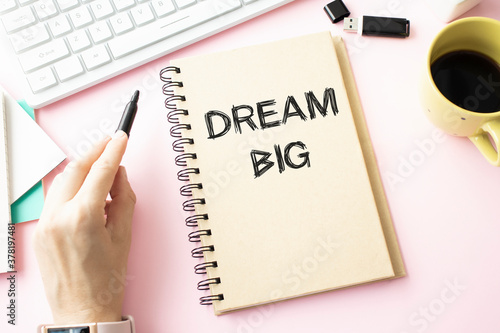 DREAM BIG on notebook on wooden desk with cup of coffee and pen