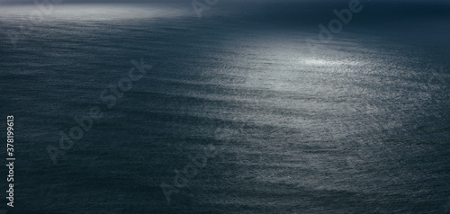 View of dappled sunlight on ocean waves and surf at dusk