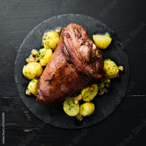 Canvas Print Baked pork leg with potatoes on a black stone plate