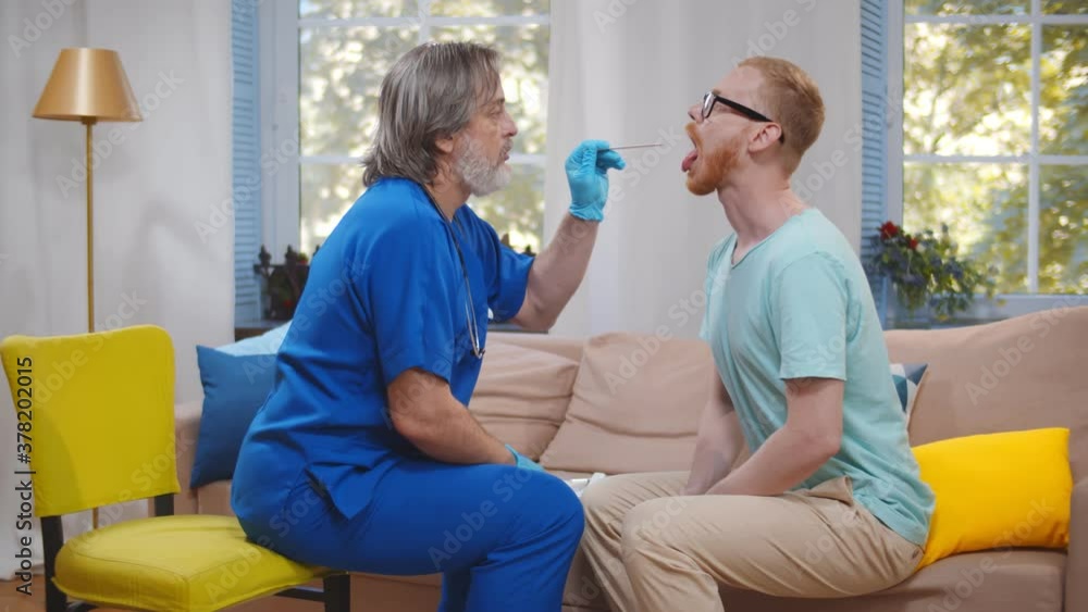 Senior doctor using tongue depressor to examine man throat during home visit Senior doctor using tongue depressor to examine man throat during home visit