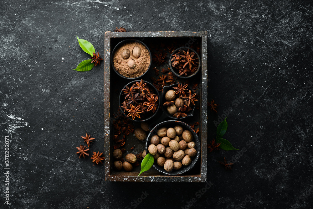 Set of fragrant Indian spices on black stone background. Nutmeg and Anise in bowls. Top view. Free space for your text.