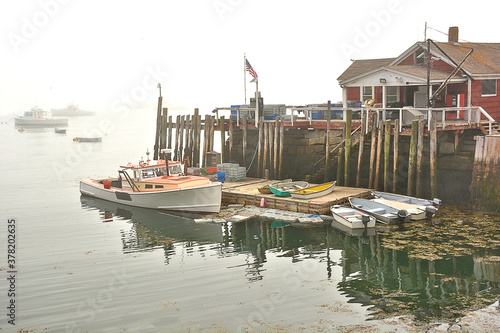 Foggy morning in coastal Maine. Lobster boat docked alongside wharf on Spruce Head Island. American flag flying.