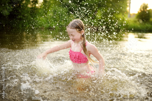 Cute little girl wearing swimsuit playing by a river on hot summer day. Adorable child having fun outdoors during summer vacations.