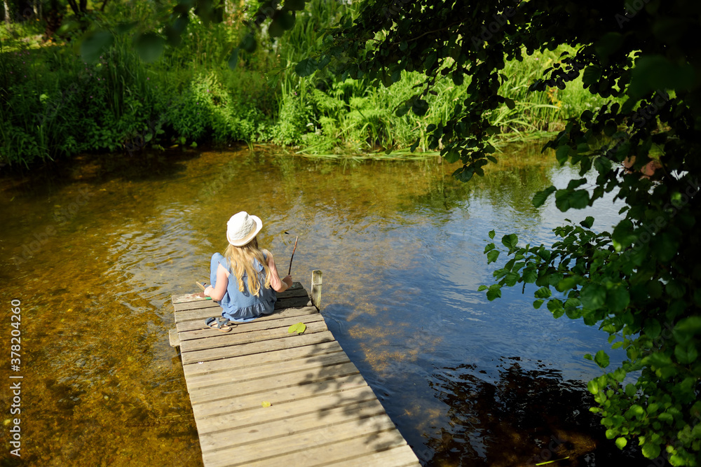 Cute young girl sitting on a pier by Pastovis lake in Moletai town, one of the oldest settlements in Lithuania and a popular resort for the inhabitants of Vilnius. Cute young girl sitting on a pier by Pastovis lake in Moletai town, one of the oldest settlements in Lithuania and a popular resort for the inhabitants of Vilnius.