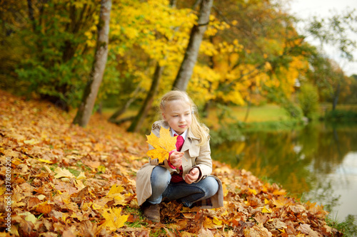 Adorable young girl having fun on beautiful autumn day. Happy child playing in autumn park. Kid gathering yellow fall foliage.