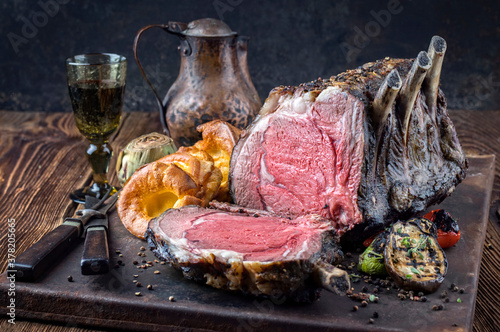 Traditional barbecue dry aged angus cote de boeuf with Yorkshire pudding and vegetable offered as close-up on a rustic board