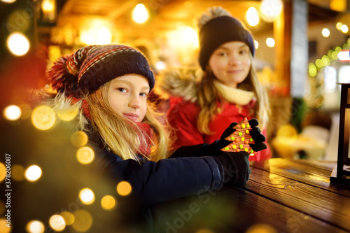 Two adorable sisters having a good time together on traditional Christmas fair in Riga, Latvia. Children enjoying sweets, candies and gingerbread on Xmas market.