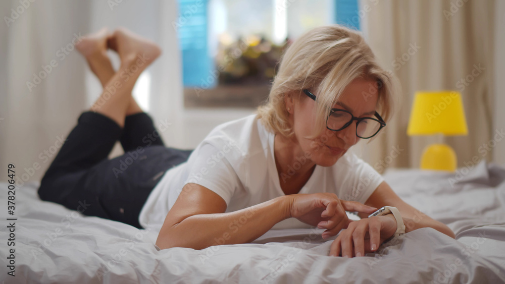 Senior woman using smartwatch relaxing on bed at home Senior woman using smartwatch relaxing on bed at home