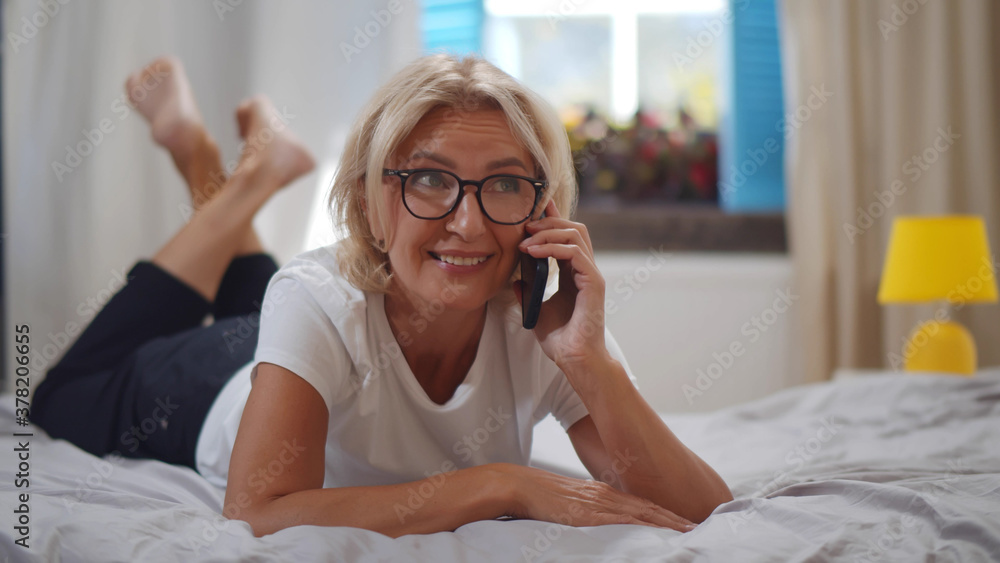 Senior woman lying on bed making phone call in bedroom at home Senior woman lying on bed making phone call in bedroom at home