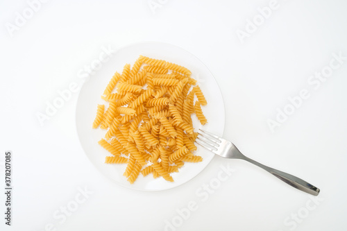 Raw uncoocked pasta fusilli in white ceramic plate with a folk isolated on white, italian cousine concept