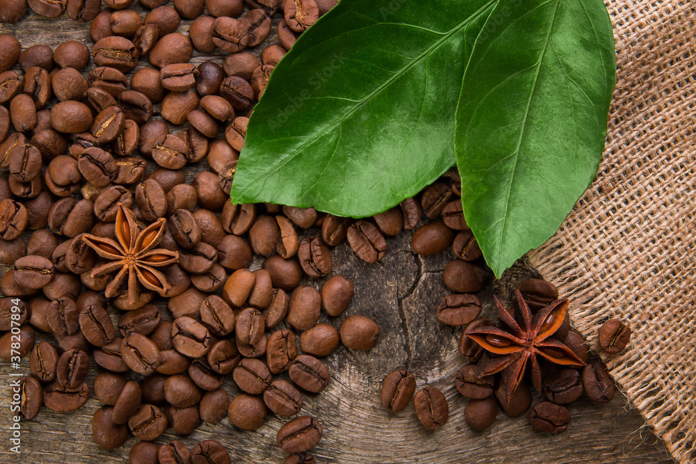 Coffee beans on a wooden background with green leaves and anise stars, close-up texture Coffee beans on a wooden background with green leaves and anise stars, close-up texture
