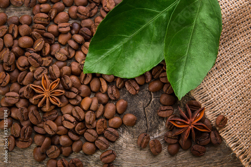 Coffee beans on a wooden background with green leaves and anise stars, close-up texture