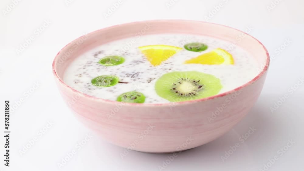 Rotating of yogurt with kiwi, gooseberry, chia in ceramic bowl on white background. Side view, close up. Rotating of yogurt with kiwi, gooseberry, chia in ceramic bowl on white background. Side view, close up.