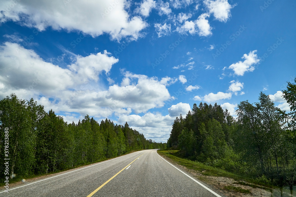 View from relief car windscreen on the blue sky with white clouds, grey asphalt road and landscape with forest and green teeses. Landscape through window