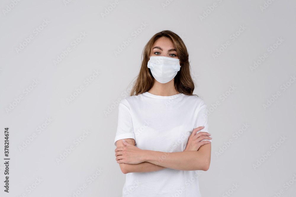 Studio portrait of young woman wearing a face mask, looking at camera, close up, isolated on gray background. Flu epidemic, protection against virus