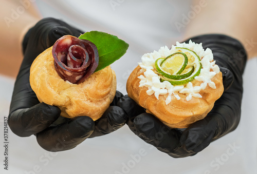 A waiter in black gloves holds a festive snack to the banquet table. Eclairs with homon and cheese. Close-up. photo